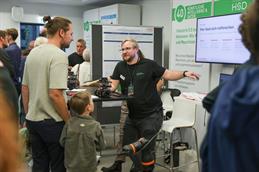 Ein HSD-Wissenschaftler erklärt einem Besucher und einem Kind kleine mobile Roboter an einem Stand zu Künstlicher Intelligenz und Daten.